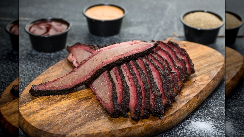 Beef brisket sliced on a wooden serving board with sauces