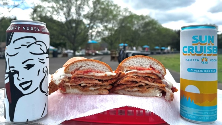 Chicken Parmesan sandwich sliced in half with two canned drinks