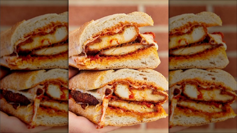 Hand holding sliced chicken Parmesan sub