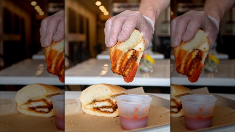 Hand dipping chicken Parmesan sandwich into marinara sauce