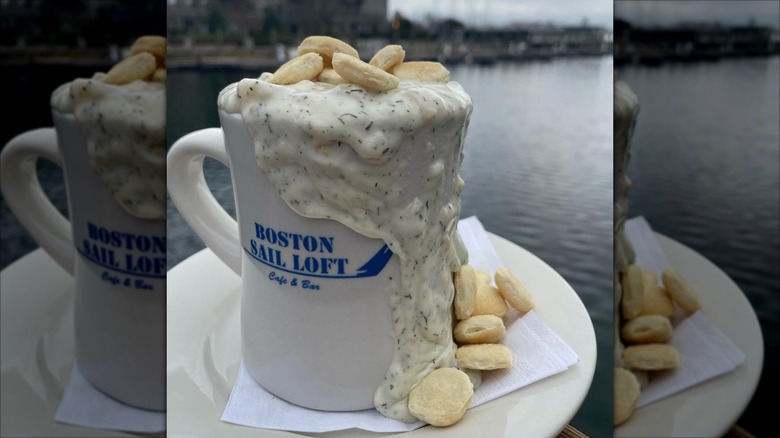Mug of Boston Sail Loft clam chowder with oyster crackers and ocean bay in the background