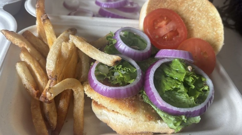 Grilled Halibut Sandwich from F Street Station topped with red onions, lettuce, and tomatoes and served with fries in a styrofoam to-go container