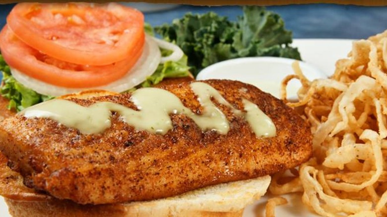 Woody's Roadside Mahi Fish Sandwich served with shoestring fried potatoes, tomatoes, onions, and lettuce on a white plate