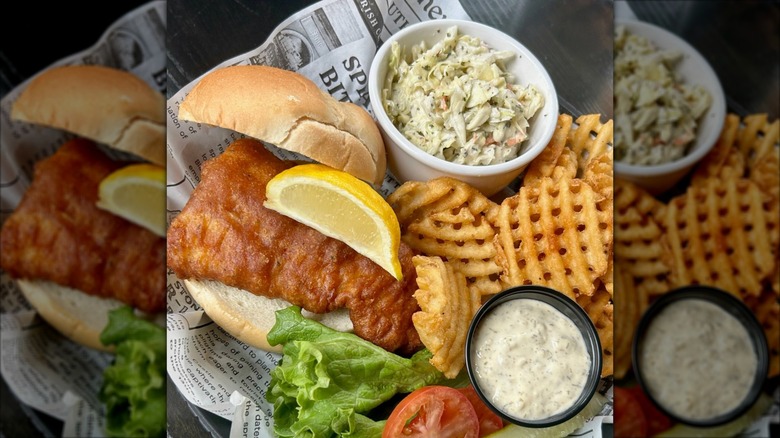 Blarney Stone Pub Fibbers Fish Sandwich garnished with lemon wedge and served with coleslaw, waffle fries, and tartar sauce on butcher paper