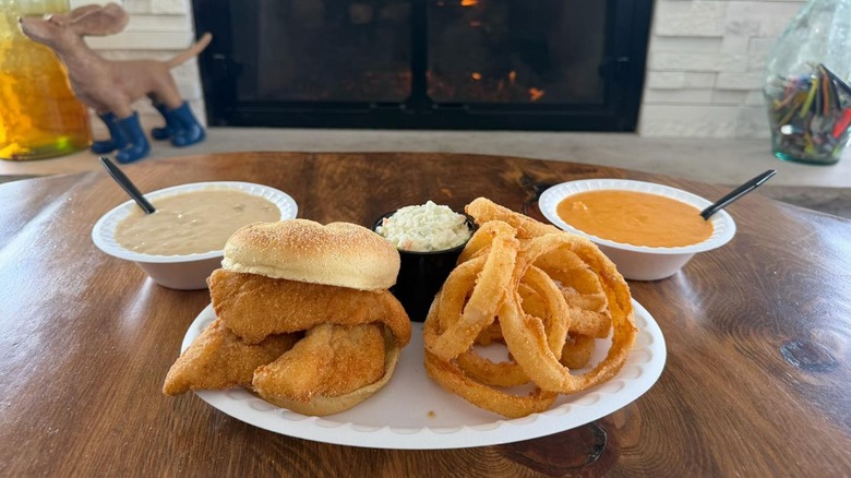Jolly Roger's Perch Sandwich with onion rings, coleslaw, and two sauces on a paper plate