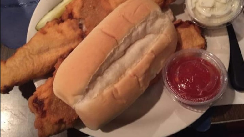 Big Jim's Fish Sandwich servied with two sauces and a pickle slice on a white plate