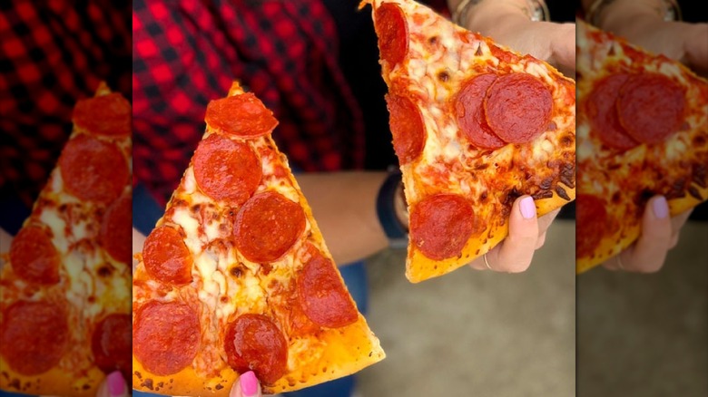 A person holds two Speedway pepperoni pizza slices, one in each hand