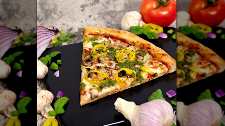 A piece of Weigel's garden harvest pizza sits on a countertop surrounded by vegetables