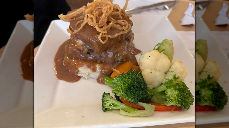 Meatloaf with brown gravy and vegetables on white square plate