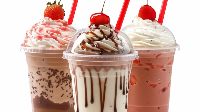 Milkshakes of different flavors in plastic take away cup, topped with whip cream and cherries