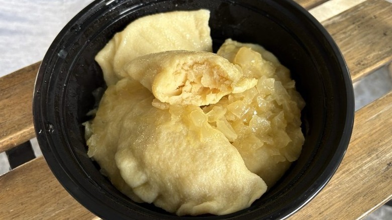 Six boiled potato pierogi with caramelized onions in a black takeout container set on an outdoor wood table