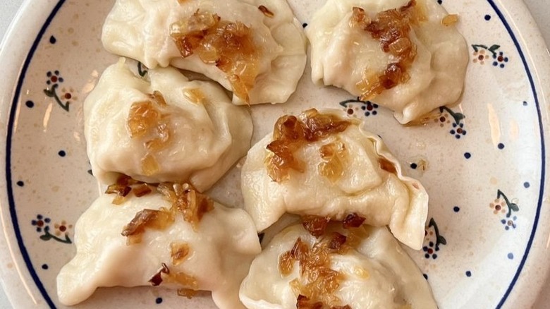 Six boiled pierogi, topped with caramelized onions, on a white European-style plate with blue dots and blue and yellow flowers on it