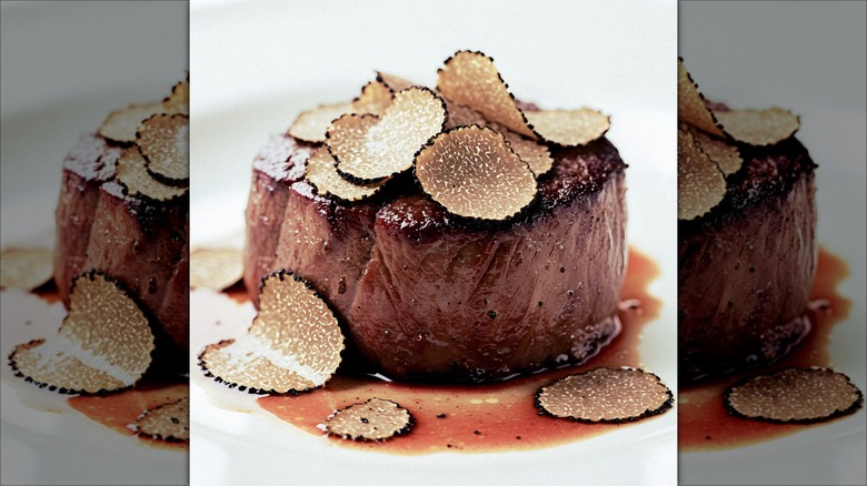A beautifully presented filet mignon topped with delicate truffle slices, served in a rich sauce, ideal for gourmet dining.