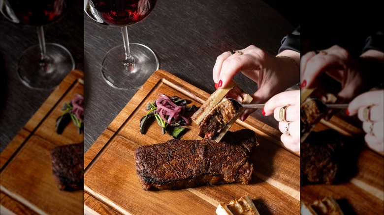 close-up of a woman's hands scraping bone marrow onto a prepared steak
