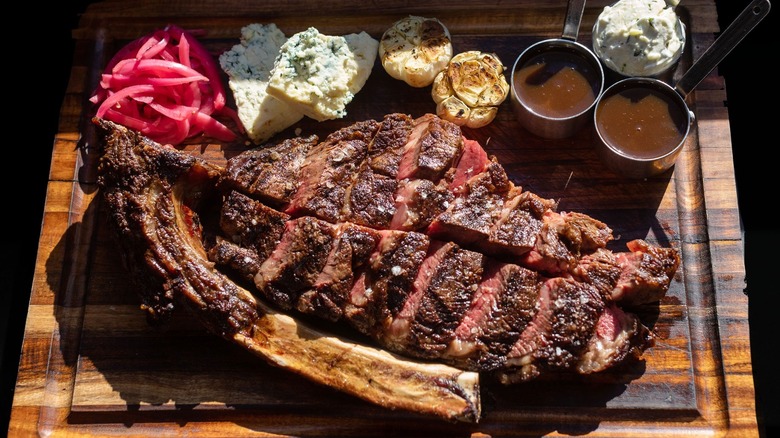 sliced steak on a cutting board with pickled onions, blue cheese, roasted garlic, and sauce