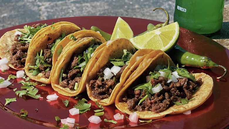 Beef tacos with onions and cilantro on plate with soda in the background