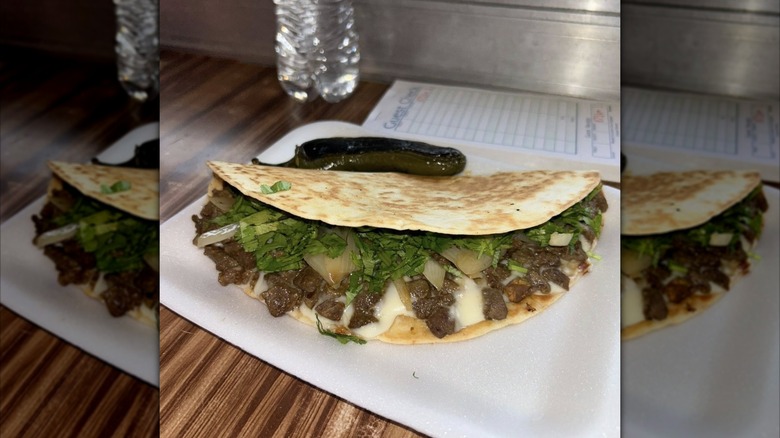 Steak taco with grilled onion and cilantro and a pepper on styrofoam plate