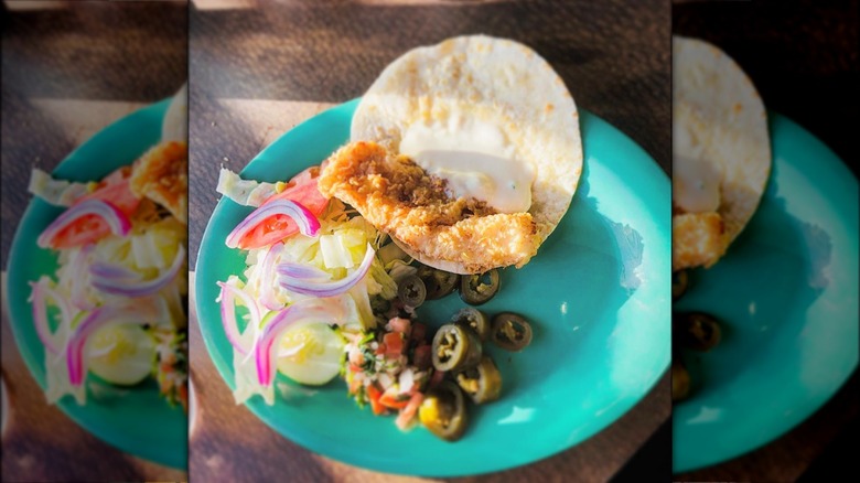 A blue plate with a fish taco and vegetables