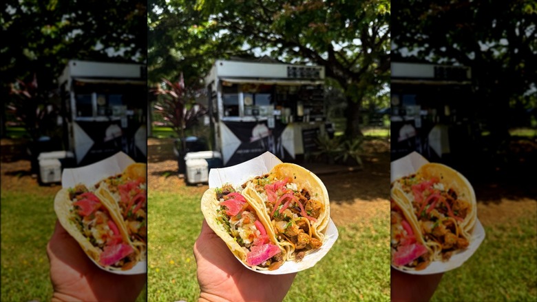 A hand holding tacos topped with red onions
