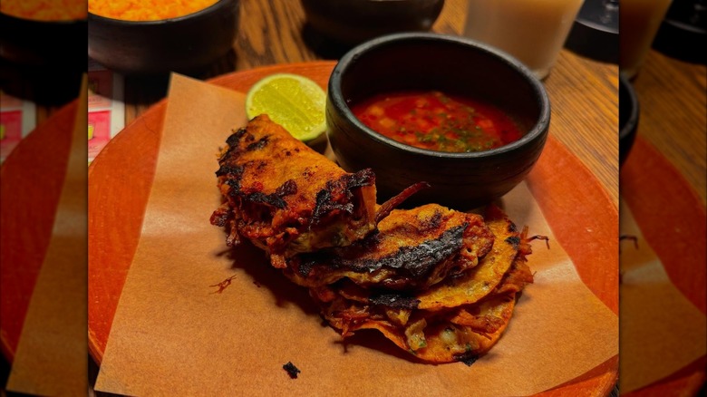Three tacos on a plate with sauce and lime
