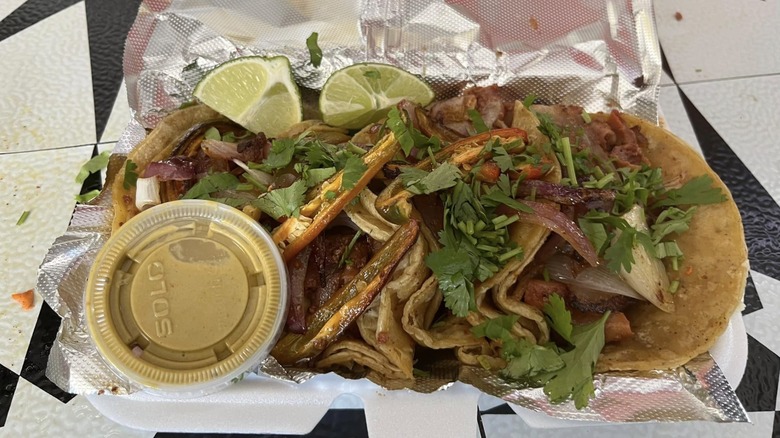 A variety of tacos with toppings, sauce and lime wedges on the side sitting on a plate