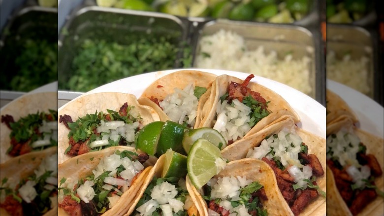 A plate of different soft shell tacos with toppings and lime