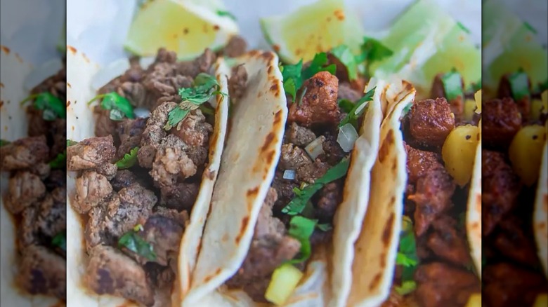 A trio of different tacos with cilantro and onions and lime wedges