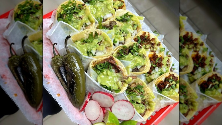 A red tray of tacos with green sauce and grilled green peppers