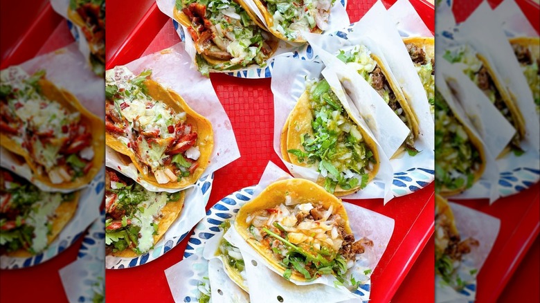 A red tray full of tacos with different toppings and salsas