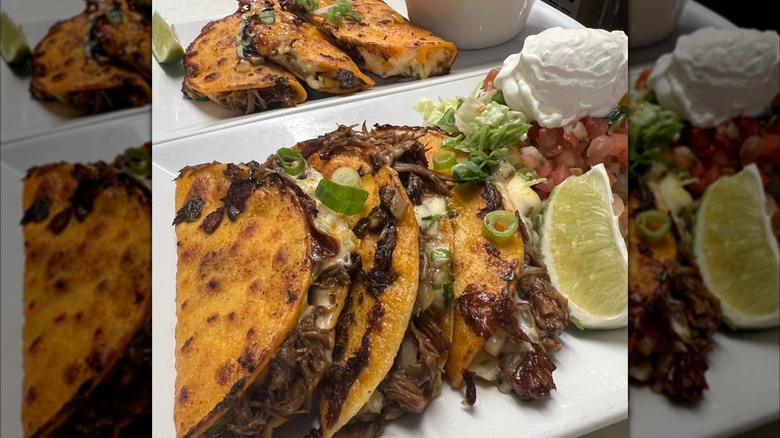 Birria tacos on plate with sour cream, salsa, and lime wedge on the side
