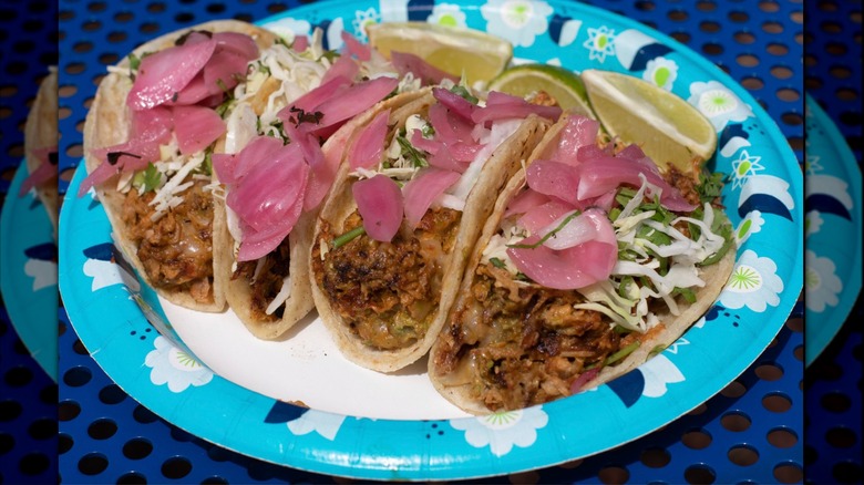 Four tacos on paper plate with pickled onions, and cilantro