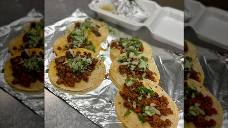 Four tacos on top of tin foil with cilantro and onions