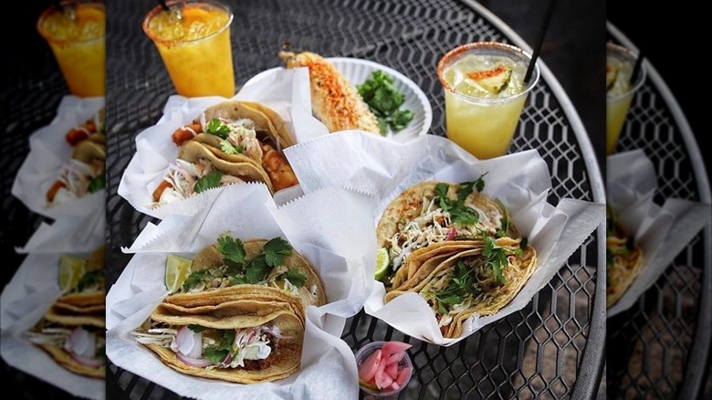 Tacos on an outside table with drinks and plate of corn on the cob