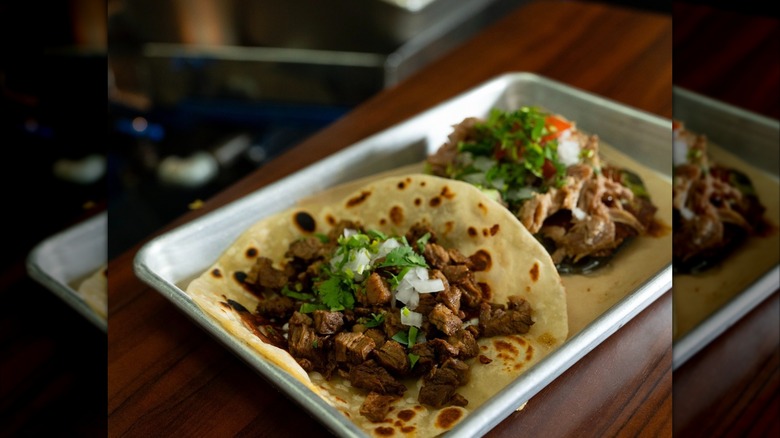 Two tacos on a metal tray on wooden table
