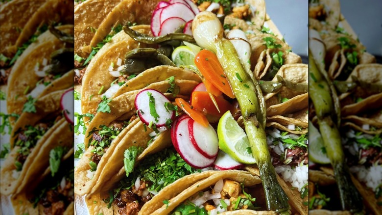 Row of tacos with radishes, lemons, and multiple veggie toppings