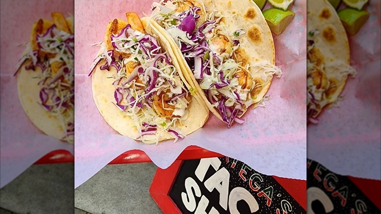 Shrimp tacos with red cabbage in red basket with wax paper with lime wedges