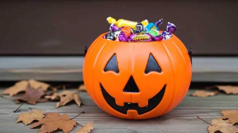 Halloween candy bucket filled with candy on wood porch with leaves