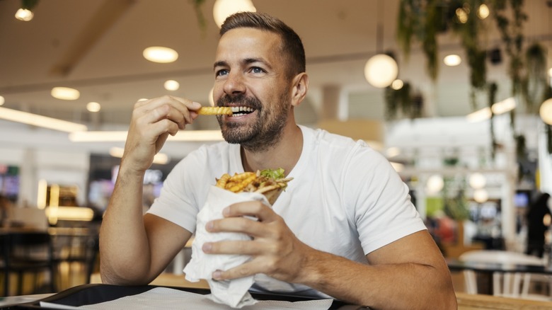 Happy adult man smiling while enjoying a gyros with french fries at a casual fast food restaurant