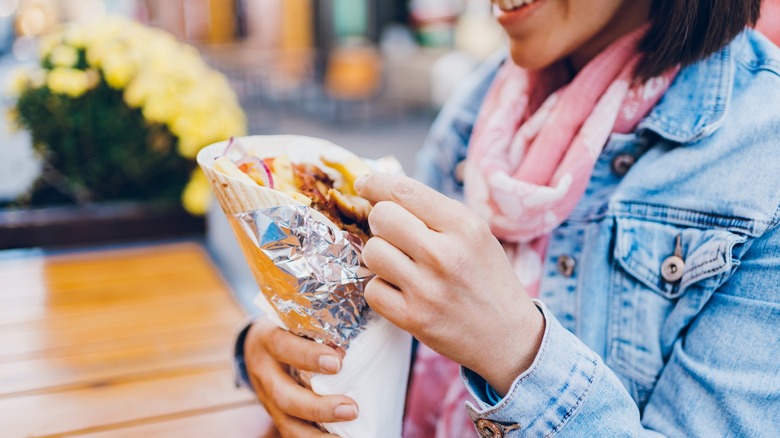 A young woman enjoys eating gyros in a cafe garden