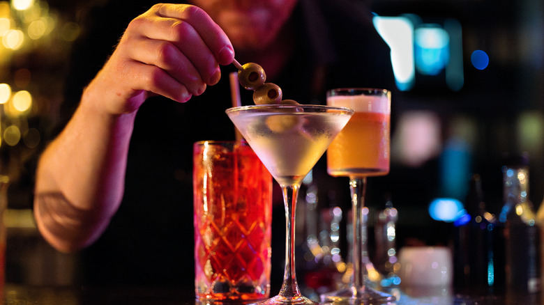 A man garnishing a dry martini with cocktail olives at a bar