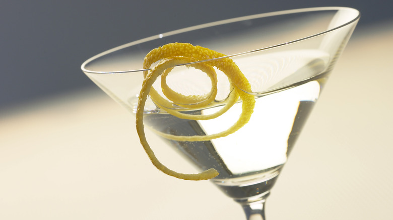 A closeup of a dry martini with a long strip of lemon peel