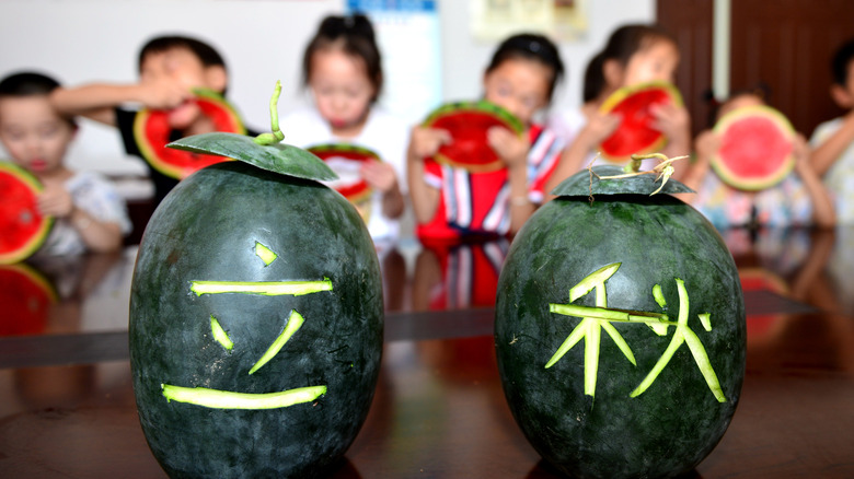Chinese characters carved into watermelon rinds with children eating watermelon in the background