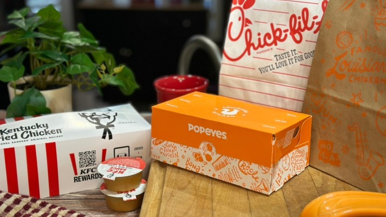 KFC, Chick-fil-A and Popeyes to go boxes and bags on wooden board