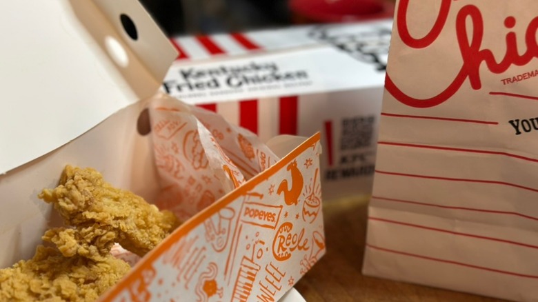 KFC, Chick-fil-A & Popeyes to go bags and boxes, Popeyes takeout box open with chicken tenders inside