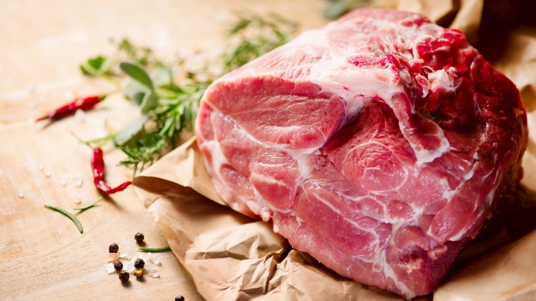 A raw pork roast near herbs on butcher paper