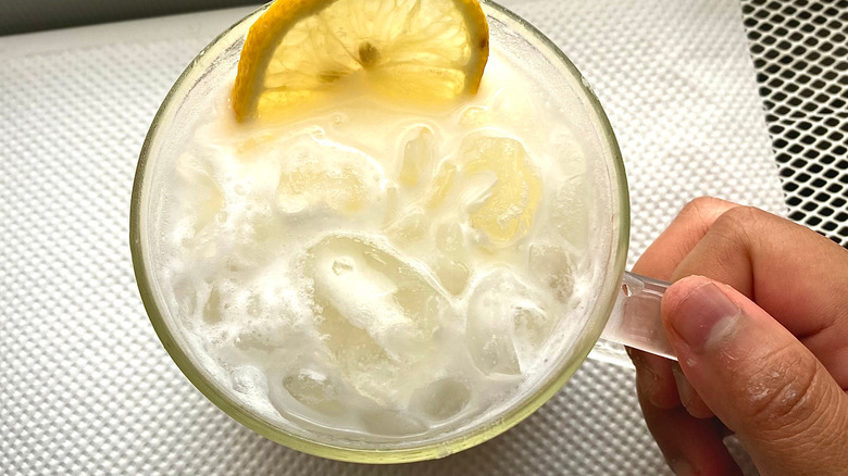 top-down view of a person holding a glass of whipped lemonade with ice and a lemon slice in it.
