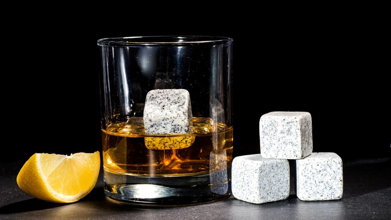 Glass of whiskey next to whiskey stones and lemon wedge