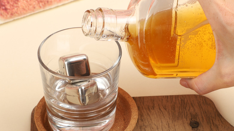 Hand pouring bottle of whiskey into glass with whiskey stones