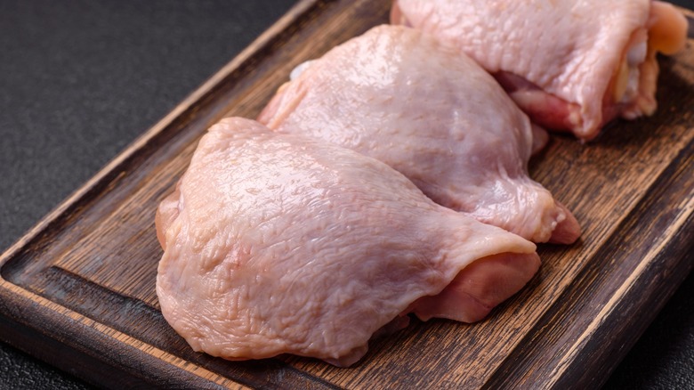 Raw skin-on chicken thighs on wood board over dark concrete background