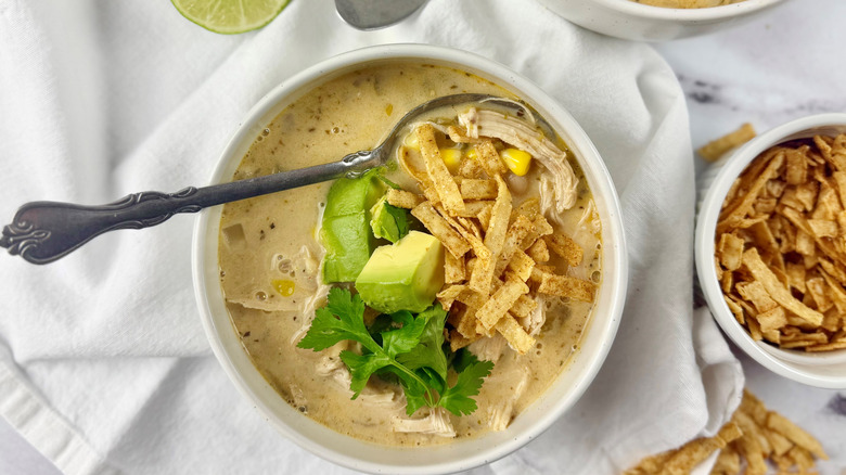 bowl of chicken chili with sliced avocado, cilantro, and tortilla strips